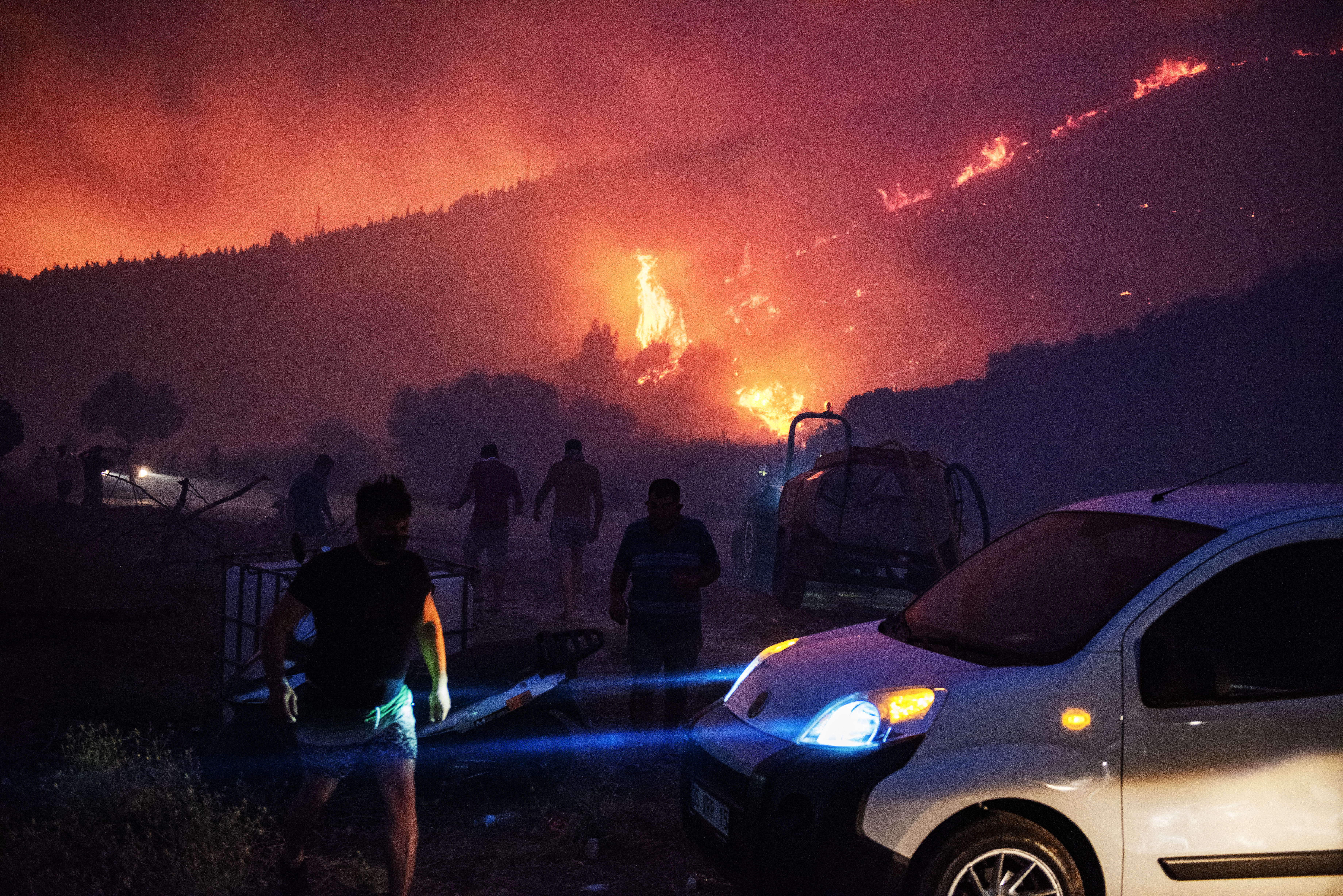 TOPSHOT - People and firefighters attempt to extinguish the flames as smoke and flares rise from a forested area following a wildfire in the Seferihisar district of Izmir, Turkey, on June 30, 2025